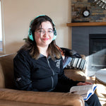 Girl smiling, wearing noise canceling headphones while holding a book